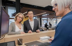 Bank teller at computer helping couple at bank branch counter