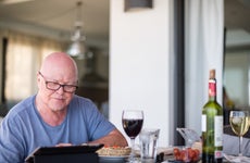 An older man researches online while having a glass of wine.