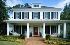 white home with flowerbeds, brick walkway and front porch with rocking chairs